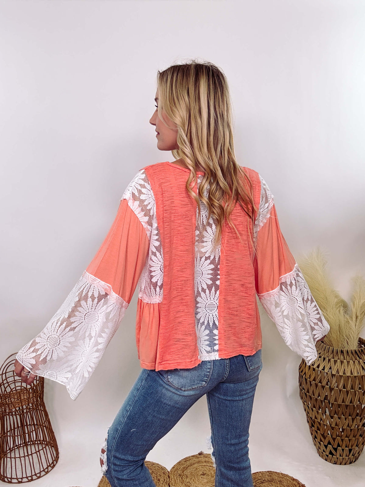 POL Clothing Coral Peach Boho Lace Flare Sleeve V-Neck Top featuring sheer floral lace sleeves, bunched side details, and a relaxed fit, made from a blend of nylon, rayon, and spandex.