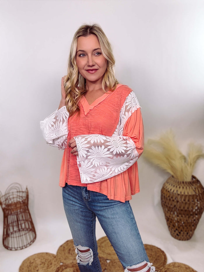 POL Clothing Coral Peach Boho Lace Flare Sleeve V-Neck Top featuring sheer floral lace sleeves, bunched side details, and a relaxed fit, made from a blend of nylon, rayon, and spandex.