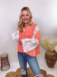 POL Clothing Coral Peach Boho Lace Flare Sleeve V-Neck Top featuring sheer floral lace sleeves, bunched side details, and a relaxed fit, made from a blend of nylon, rayon, and spandex.