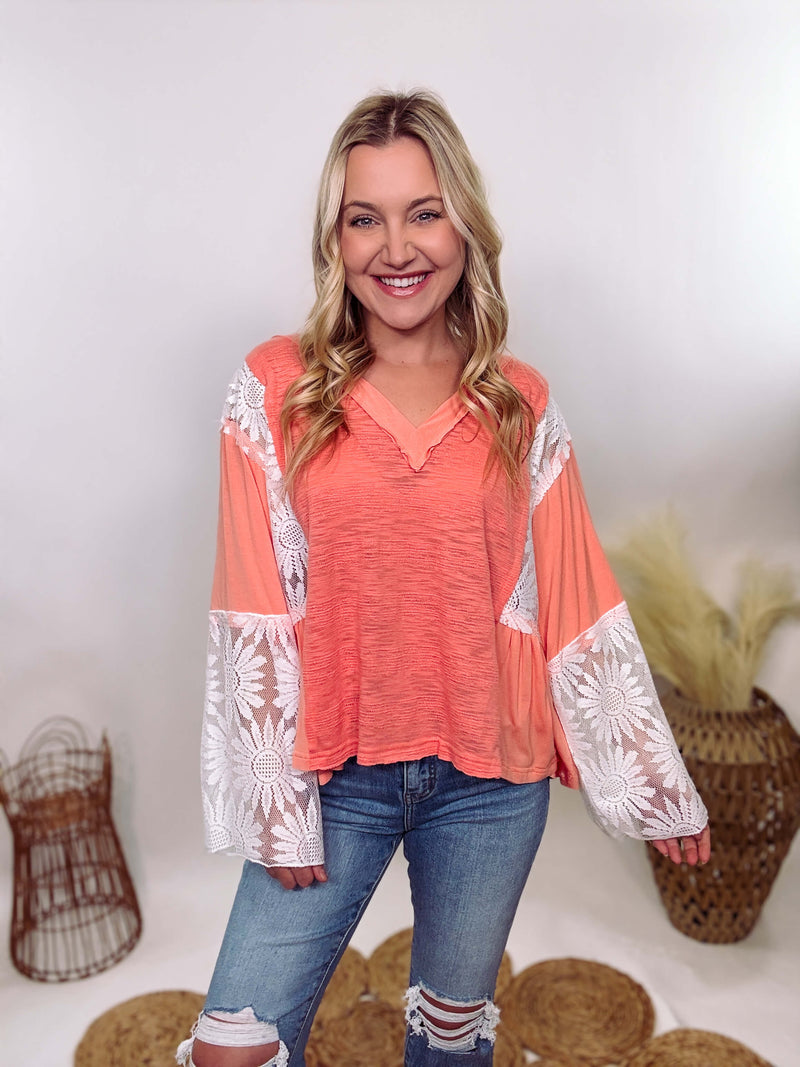 POL Clothing Coral Peach Boho Lace Flare Sleeve V-Neck Top featuring sheer floral lace sleeves, bunched side details, and a relaxed fit, made from a blend of nylon, rayon, and spandex.