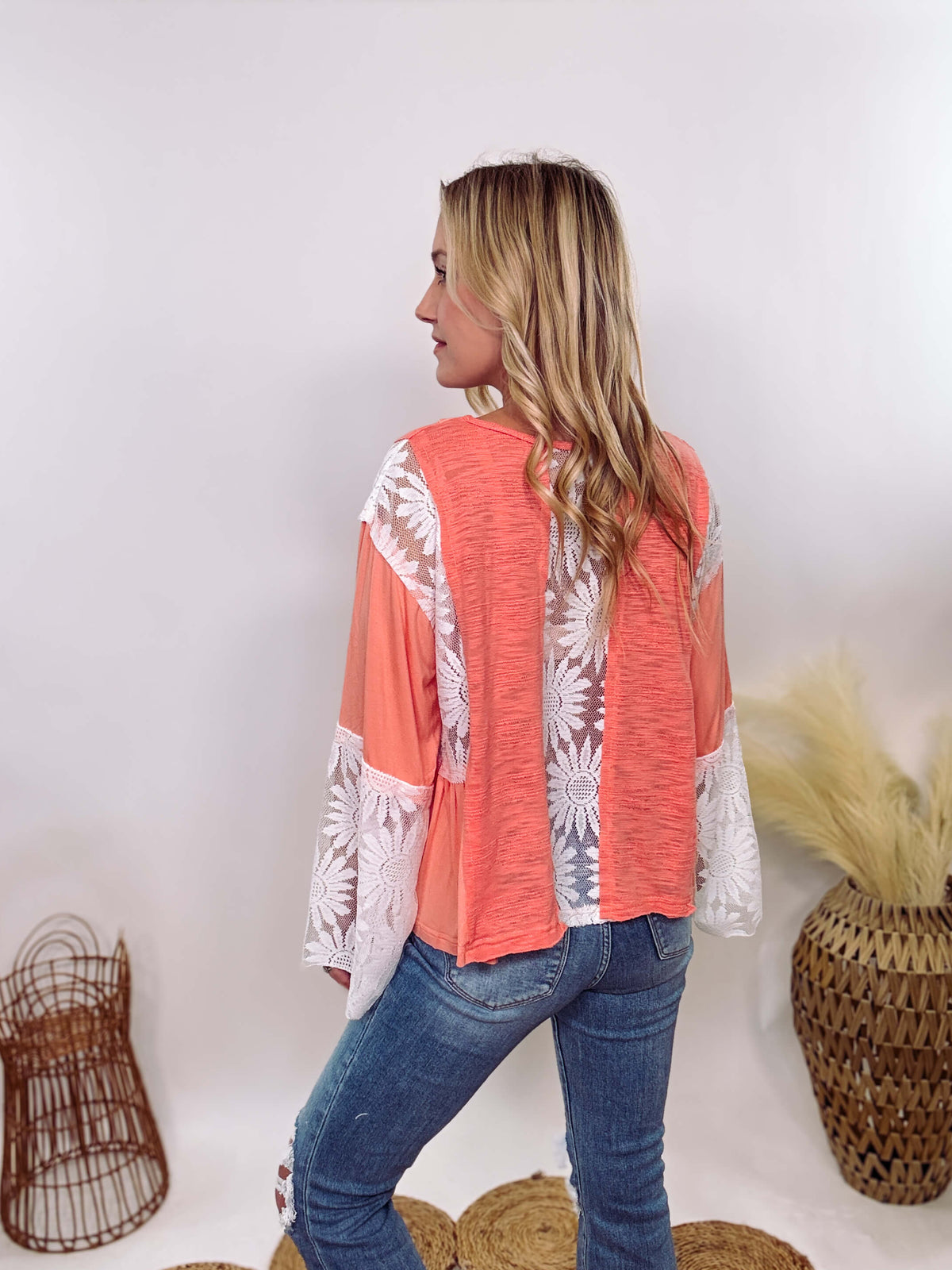 POL Clothing Coral Peach Boho Lace Flare Sleeve V-Neck Top featuring sheer floral lace sleeves, bunched side details, and a relaxed fit, made from a blend of nylon, rayon, and spandex.