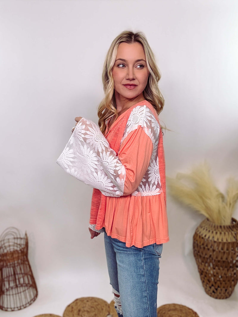 POL Clothing Coral Peach Boho Lace Flare Sleeve V-Neck Top featuring sheer floral lace sleeves, bunched side details, and a relaxed fit, made from a blend of nylon, rayon, and spandex.