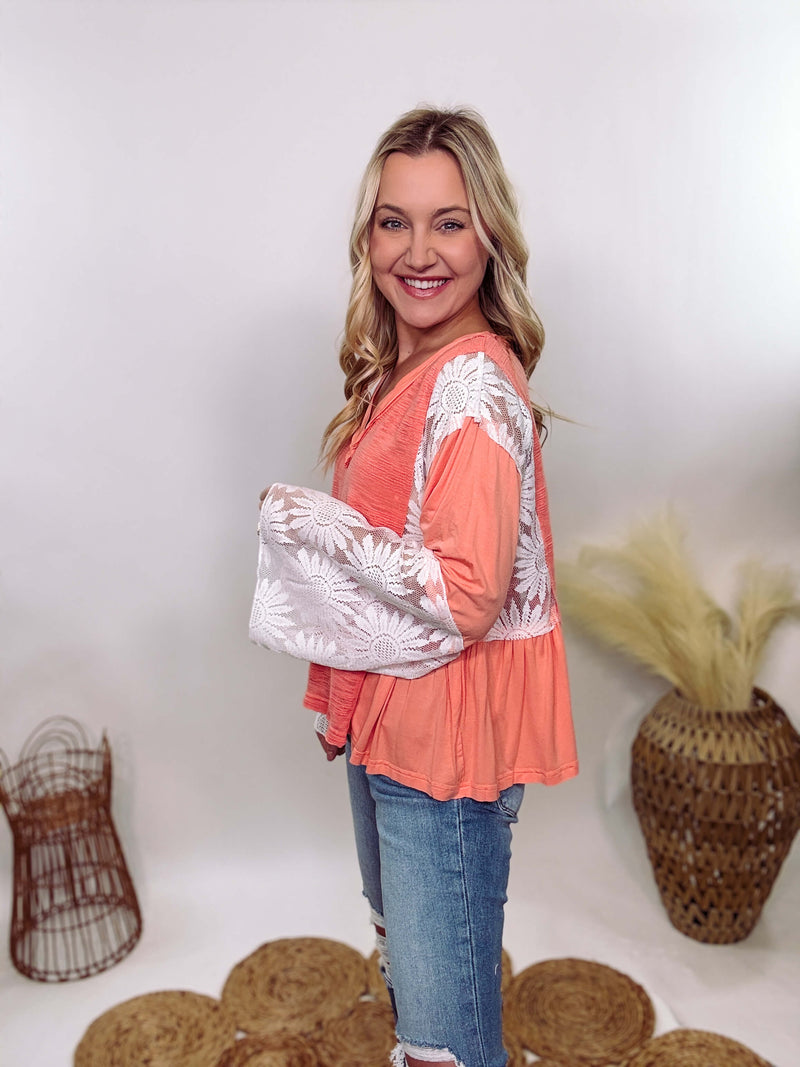 POL Clothing Coral Peach Boho Lace Flare Sleeve V-Neck Top featuring sheer floral lace sleeves, bunched side details, and a relaxed fit, made from a blend of nylon, rayon, and spandex.