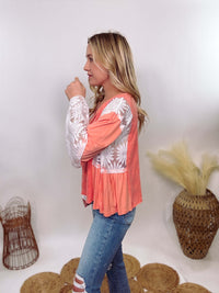 POL Clothing Coral Peach Boho Lace Flare Sleeve V-Neck Top featuring sheer floral lace sleeves, bunched side details, and a relaxed fit, made from a blend of nylon, rayon, and spandex.POL Clothing Coral Peach Boho Lace Flare Sleeve V-Neck Top featuring sheer floral lace sleeves, bunched side details, and a relaxed fit, made from a blend of nylon, rayon, and spandex.