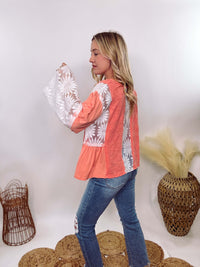 POL Clothing Coral Peach Boho Lace Flare Sleeve V-Neck Top featuring sheer floral lace sleeves, bunched side details, and a relaxed fit, made from a blend of nylon, rayon, and spandex.