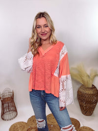 POL Clothing Coral Peach Boho Lace Flare Sleeve V-Neck Top featuring sheer floral lace sleeves, bunched side details, and a relaxed fit, made from a blend of nylon, rayon, and spandex.