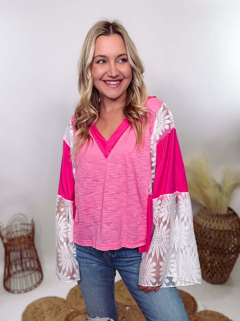 POL Clothing Hot Pink Boho Lace Flare Sleeve V-Neck Top featuring sheer floral lace sleeves, bunched side details, and a relaxed fit, made from a blend of nylon, rayon, and spandex.