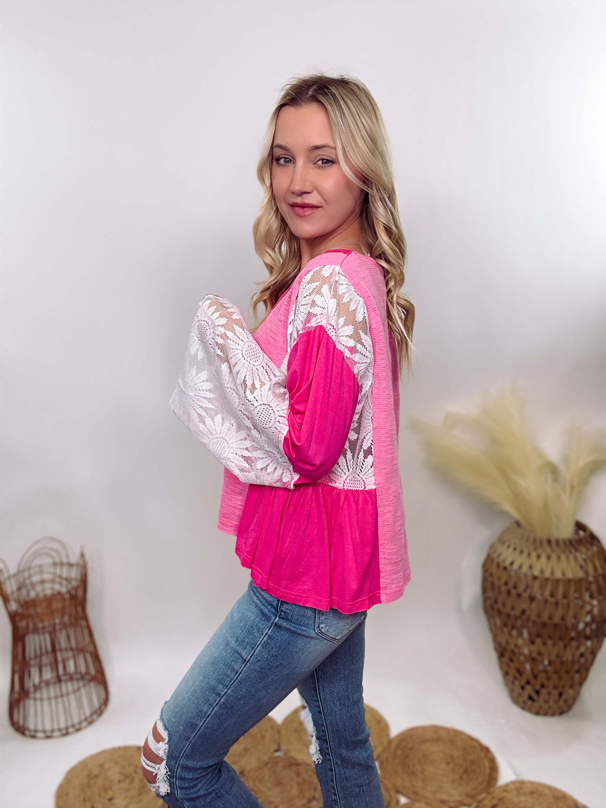 POL Clothing Hot Pink Boho Lace Flare Sleeve V-Neck Top featuring sheer floral lace sleeves, bunched side details, and a relaxed fit, made from a blend of nylon, rayon, and spandex.