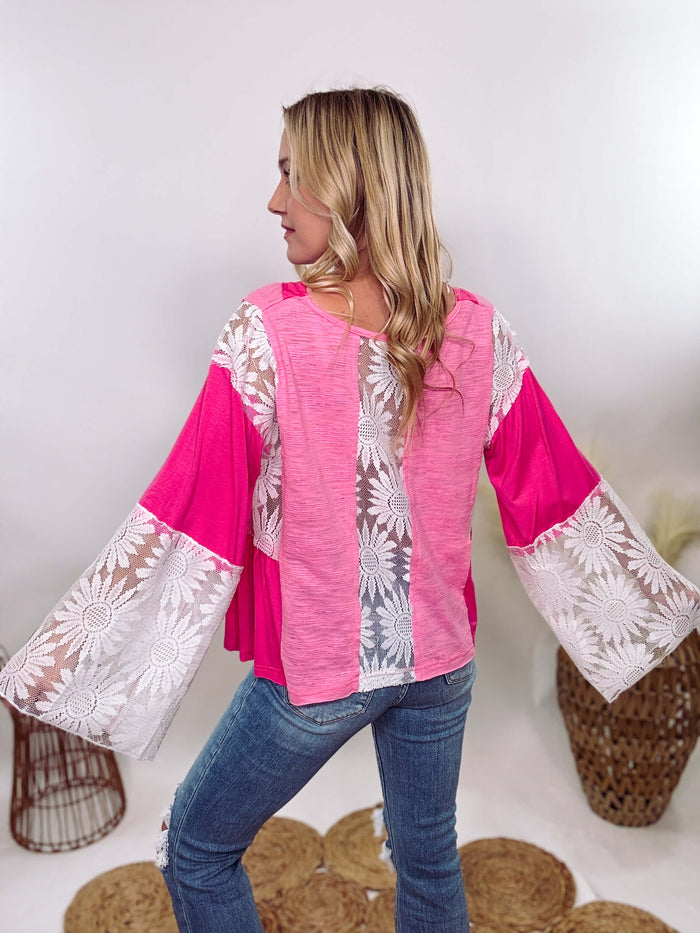 POL Clothing Hot Pink Boho Lace Flare Sleeve V-Neck Top featuring sheer floral lace sleeves, bunched side details, and a relaxed fit, made from a blend of nylon, rayon, and spandex.