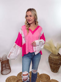 POL Clothing Hot Pink Boho Lace Flare Sleeve V-Neck Top featuring sheer floral lace sleeves, bunched side details, and a relaxed fit, made from a blend of nylon, rayon, and spandex.