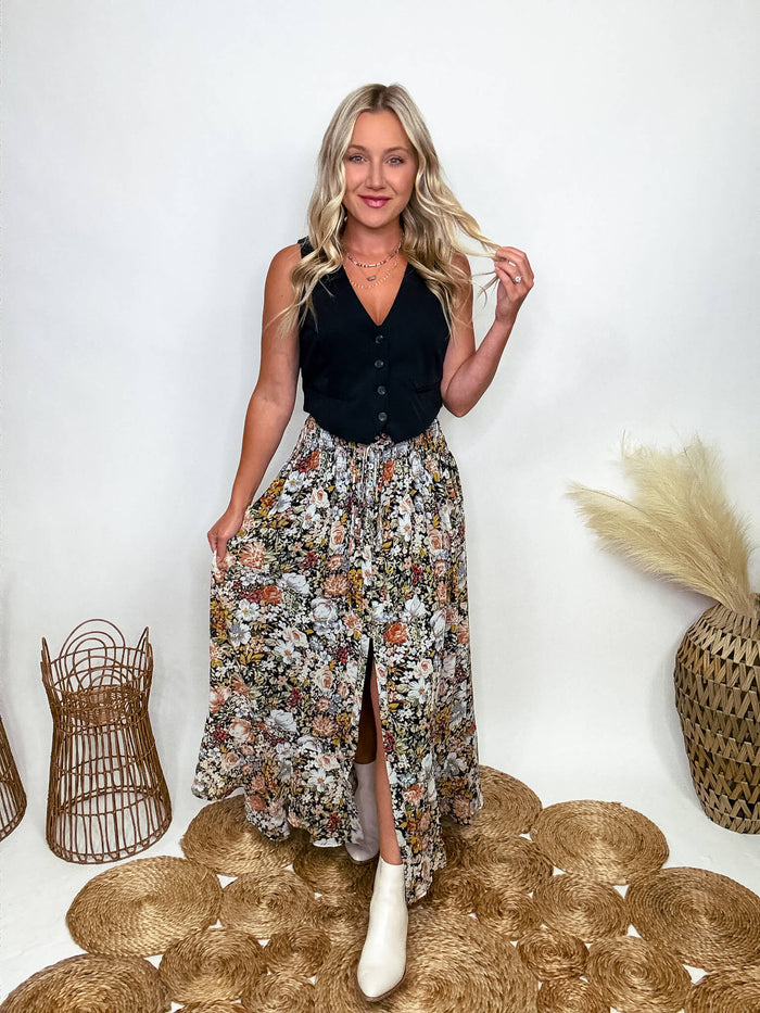 Promesa Vintage Floral Boho Maxi Skirt with Front Slit and Smocked Stretchy Waistband, Styled with Black Vest and White Booties at Bmaes Boutique