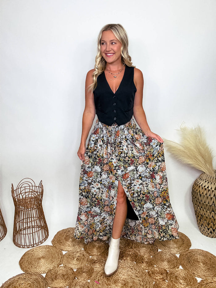 Promesa Vintage Floral Boho Maxi Skirt with Front Slit and Smocked Stretchy Waistband, Styled with Black Vest and White Booties at Bmaes Boutique