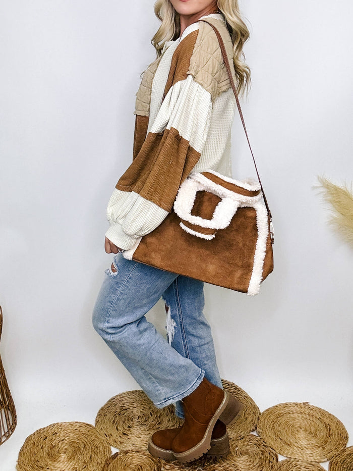 Brown faux suede cross body tote bag with sherpa-lined edges, featuring a full zip closure and adjustable strap, perfect for cozy fall and winter outings.