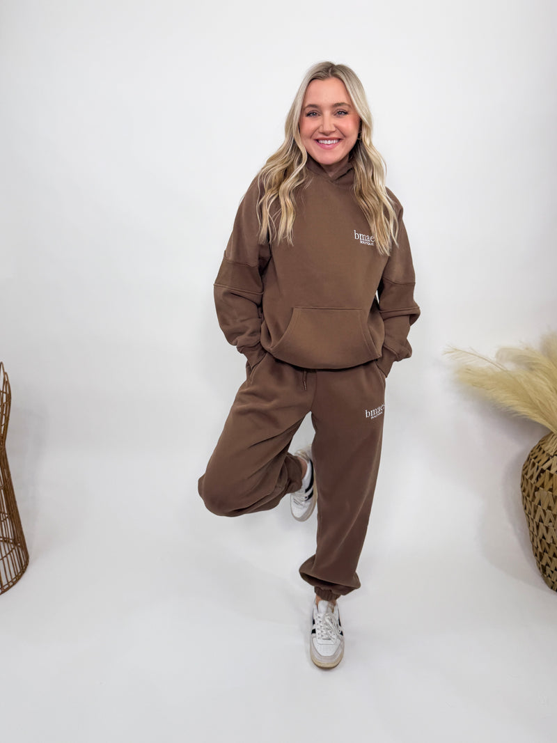 Chocolate brown fleece-lined luxury lounge Bmaes hoodie with embroidered Bmaes Boutique logo, drop shoulders, kangaroo pocket, and ribbed details. Perfect for cozy lounging or pairing with the matching joggers for a stylish, warm set from Bmaes Boutique.