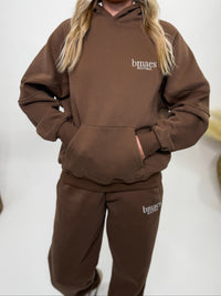 Chocolate brown fleece-lined luxury lounge Bmaes hoodie with embroidered Bmaes Boutique logo, drop shoulders, kangaroo pocket, and ribbed details. Perfect for cozy lounging or pairing with the matching joggers for a stylish, warm set from Bmaes Boutique.