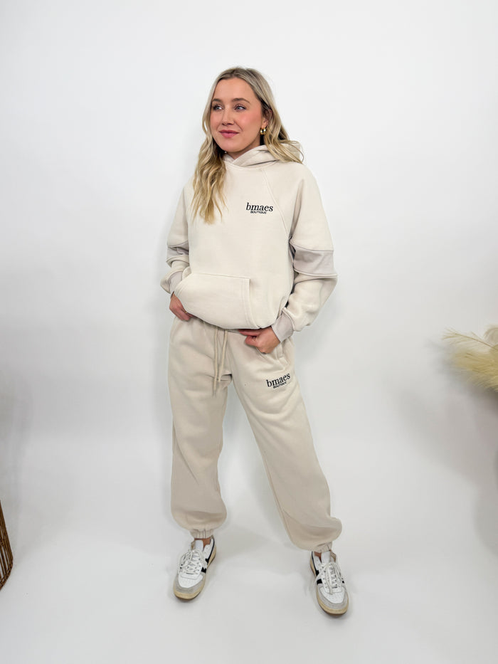 Cream fleece-lined luxury lounge Bmaes hoodie with embroidered Bmaes Boutique logo, drop shoulders, kangaroo pocket, and ribbed details. Perfect for cozy lounging or pairing with the matching joggers for a stylish, warm set from Bmaes Boutique.