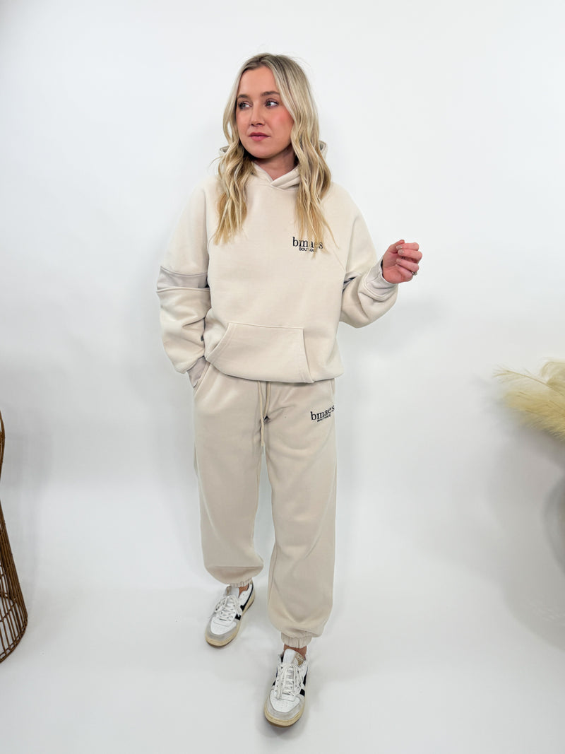 Cream fleece-lined luxury lounge Bmaes hoodie with embroidered Bmaes Boutique logo, drop shoulders, kangaroo pocket, and ribbed details. Perfect for cozy lounging or pairing with the matching joggers for a stylish, warm set from Bmaes Boutique.