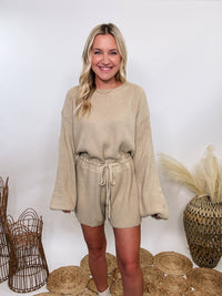 Creamy taupe long sleeve sweater romper by Mable, adjustable waist, styled with boots for fall and winter