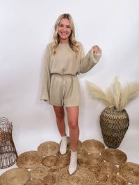 Creamy taupe long sleeve sweater romper by Mable, adjustable waist, styled with boots for fall and winter