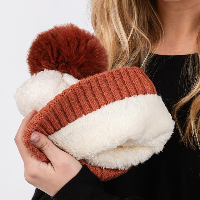 Rust-colored cuffed sherpa beanie with faux fur pom, made from 100% polyester.