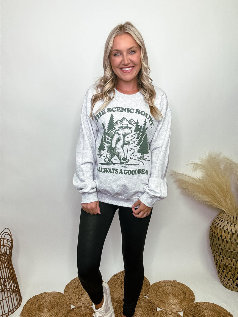 Heather grey fleece lined sweatshirt with a bear hiking graphic and the text 'The scenic route is always a good idea.' Perfect for fall outdoor activities. Model Brooke is 5'4" wearing size small.