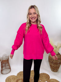 Hot pink oversized sweater with exposed seams, side slits, and a ribbed hem. Cozy, stylish, and perfect for brightening up your winter wardrobe.