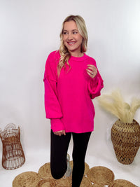 Hot pink oversized sweater with exposed seams, side slits, and a ribbed hem. Cozy, stylish, and perfect for brightening up your winter wardrobe.