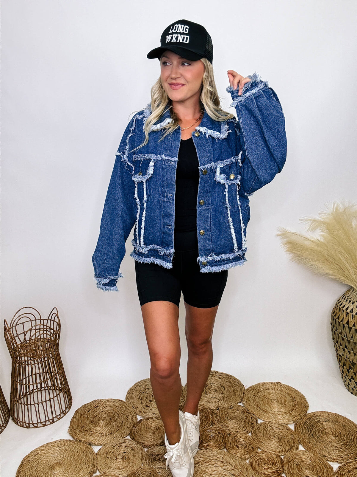 Oversized frayed hem denim jacket with exaggerated frayed hems and seams, styled over black biker shorts and a black ribbed baby tee.