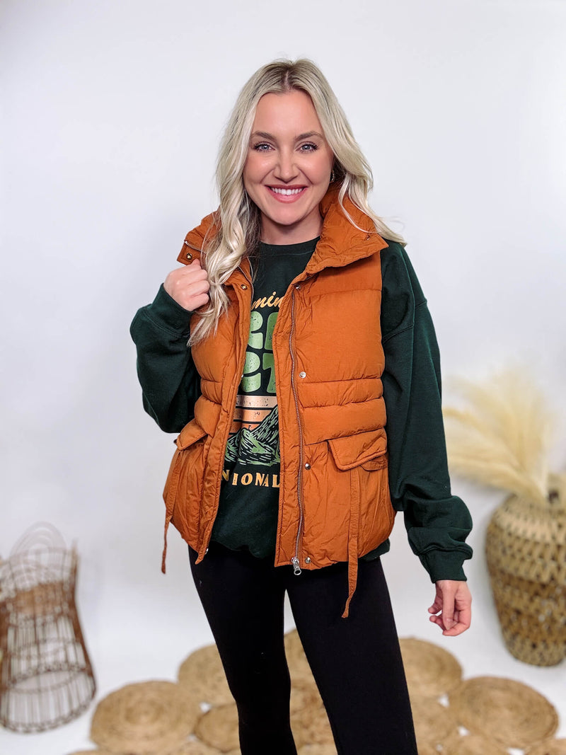 Shop the Rusty Burnt Orange Cargo Puffer Vest at Bmaes Boutique. Made from 100% polyamide, this stylish and versatile vest features two flap pockets and is perfect for layering over sweatshirts or tees.