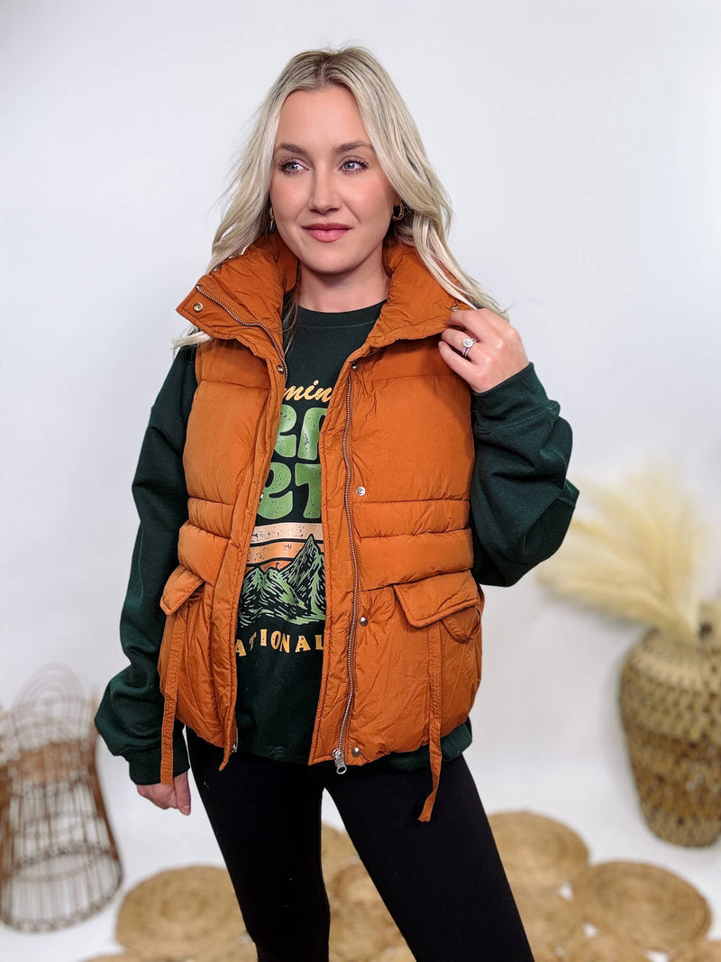 Shop the Rusty Burnt Orange Cargo Puffer Vest at Bmaes Boutique. Made from 100% polyamide, this stylish and versatile vest features two flap pockets and is perfect for layering over sweatshirts or tees.