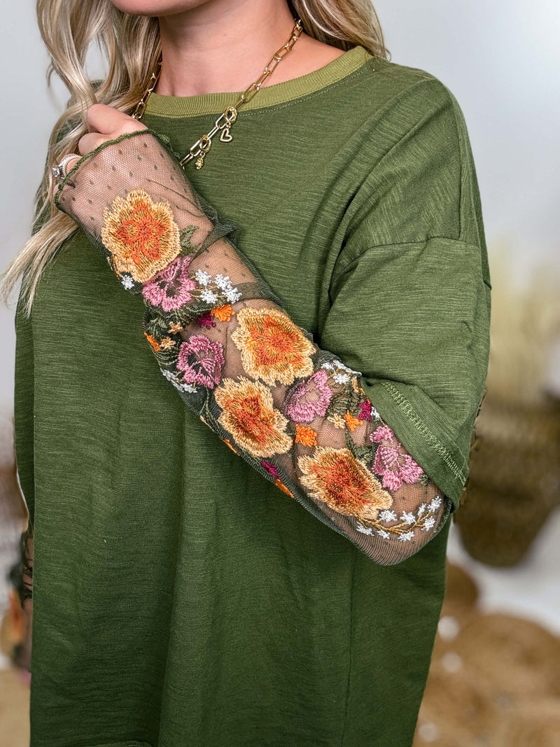 In Loom Oversized olive green tee with layered sheer embroidered floral lace mesh sleeves. Relaxed fit, earthy olive tone, and high-quality fabric blend. Perfect for casual fall outfits or dressing up with jeans or leather leggings. Feminine and edgy design ideal for crisp autumn days.