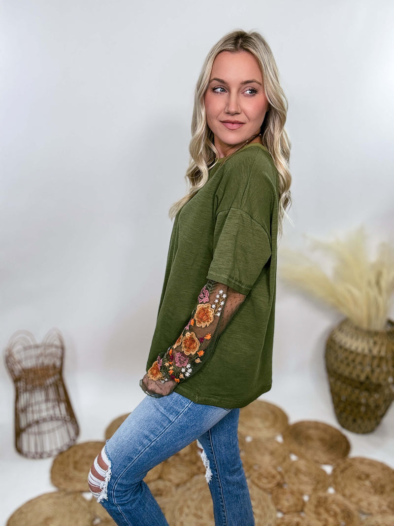 In Loom Oversized olive green tee with layered sheer embroidered floral lace mesh sleeves. Relaxed fit, earthy olive tone, and high-quality fabric blend. Perfect for casual fall outfits or dressing up with jeans or leather leggings. Feminine and edgy design ideal for crisp autumn days.