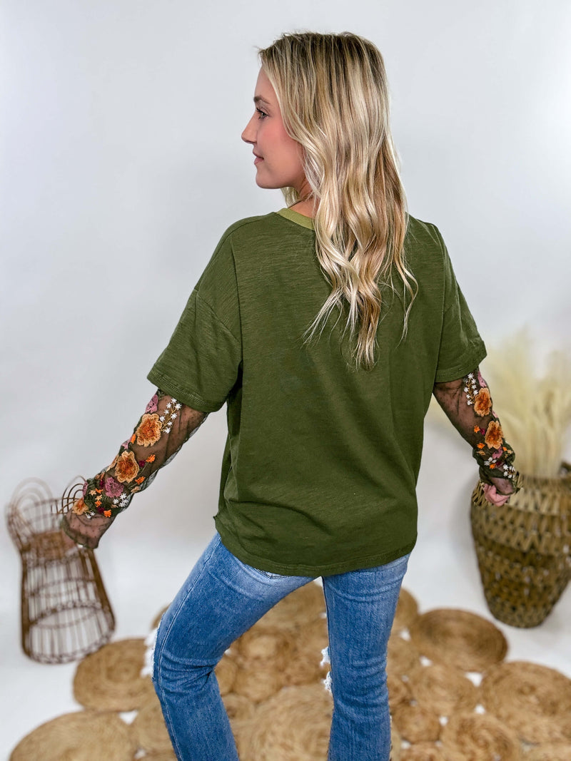 In Loom Oversized olive green tee with layered sheer embroidered floral lace mesh sleeves. Relaxed fit, earthy olive tone, and high-quality fabric blend. Perfect for casual fall outfits or dressing up with jeans or leather leggings. Feminine and edgy design ideal for crisp autumn days.