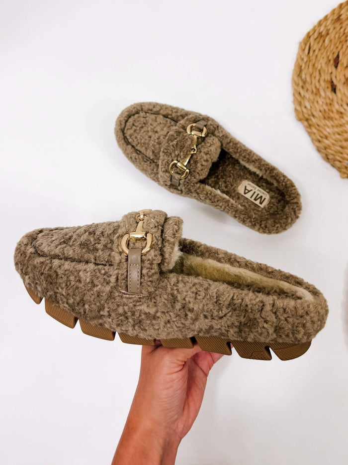 MIA limited edition cocoa faux sherling slipper mule. Cocoa faux shearling mules with fur lining, gold buckle accent, and rubber outsole, ideal for lounging or casual outings.