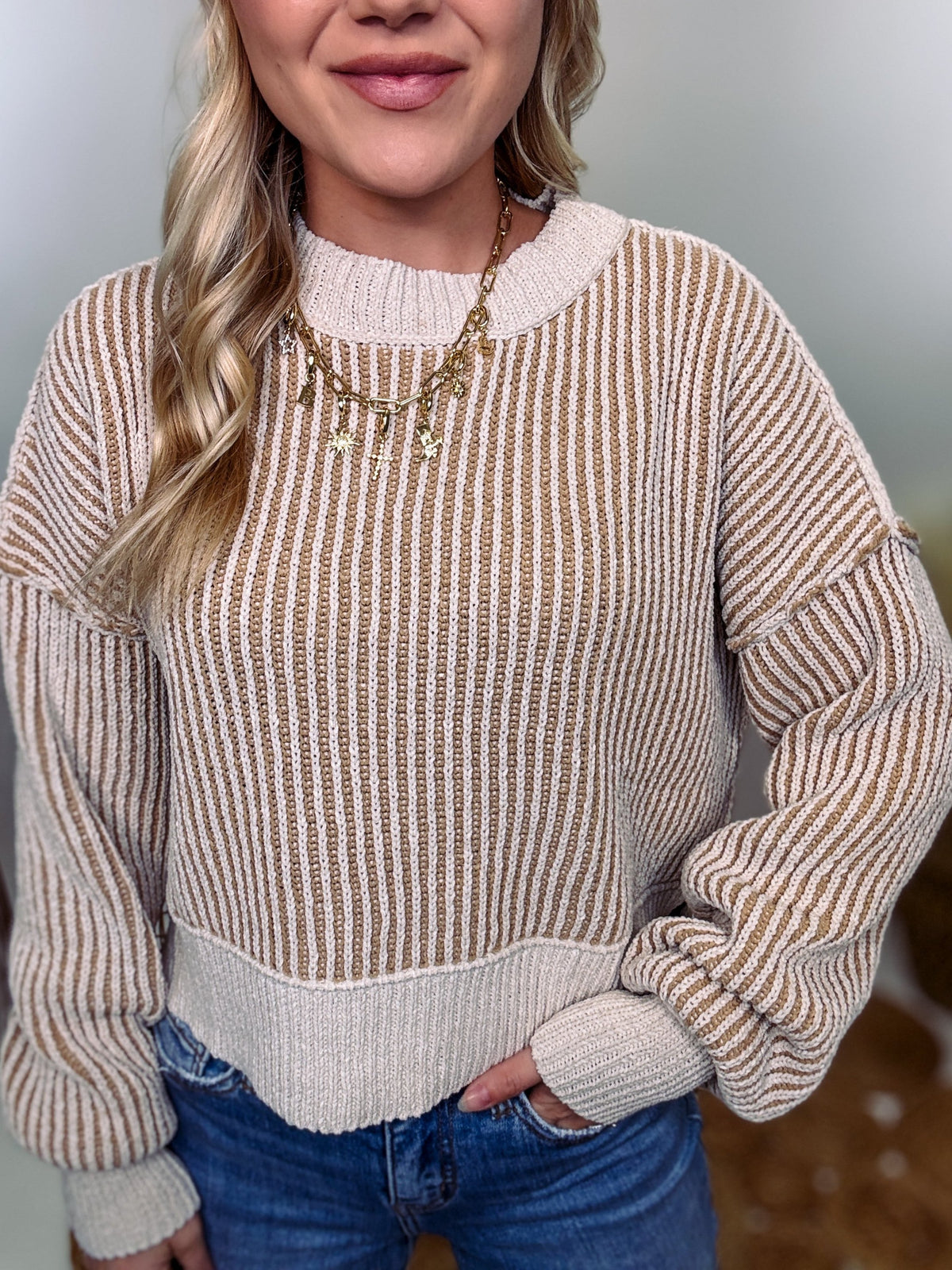 Two-tone neutral ribbed sweater featuring a cream body with light brown ribbed detailing, round neck, and loose fit. Made from 100% polyester with a soft, non-scratchy feel. Styled with a neutral beanie and kick flare denim for a cozy winter look.