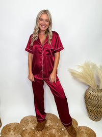 Burgundy satin pajama set featuring a button-down short sleeve shirt and long pants with an elastic waist, true to size relaxed fit. Model Brooke is 5'4" wearing size small.