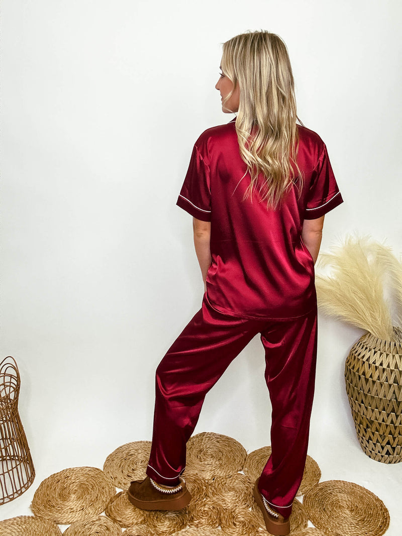 Burgundy satin pajama set featuring a button-down short sleeve shirt and long pants with an elastic waist, true to size relaxed fit. Model Brooke is 5'4" wearing size small.