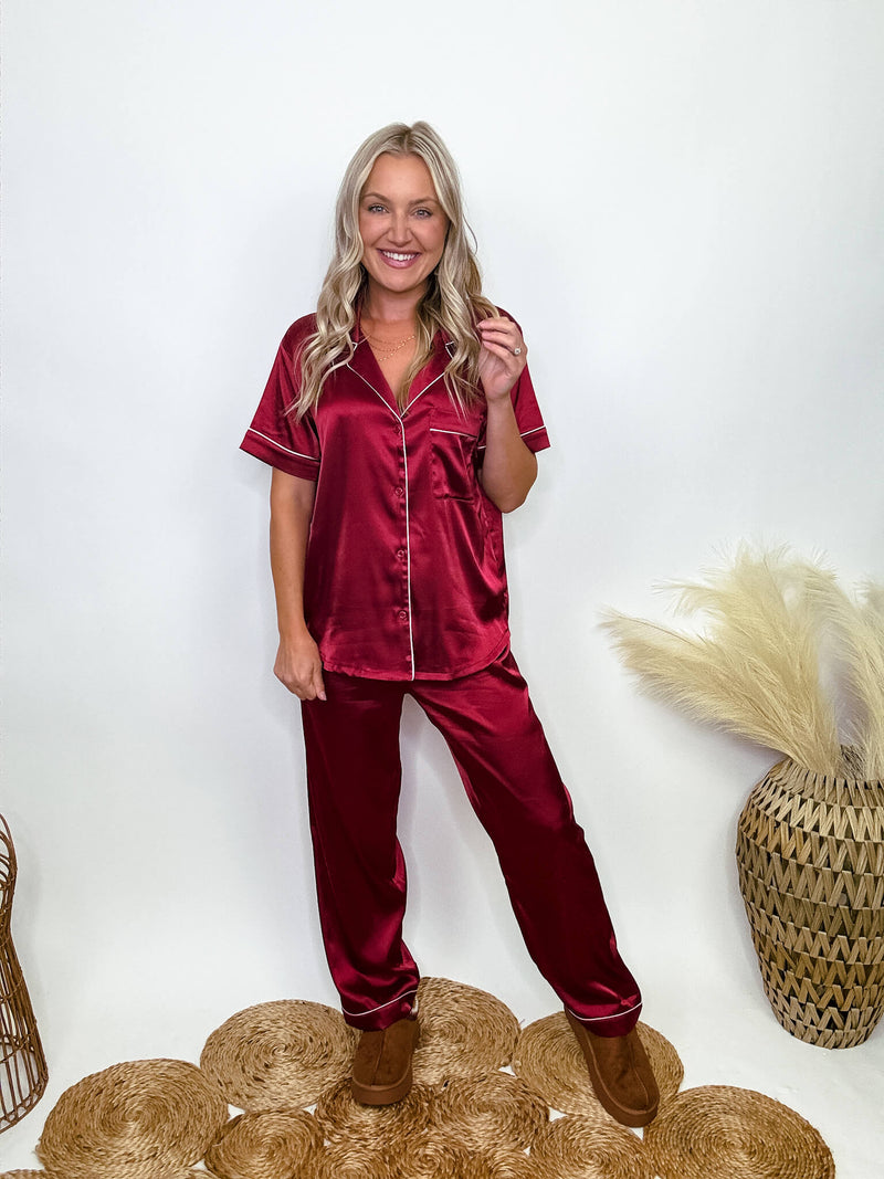 Burgundy satin pajama set featuring a button-down short sleeve shirt and long pants with an elastic waist, true to size relaxed fit. Model Brooke is 5'4" wearing size small.