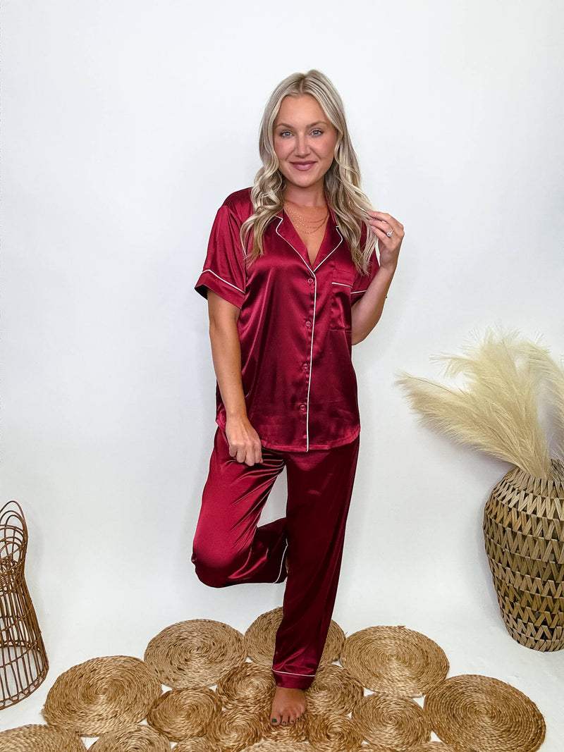 Burgundy satin pajama set featuring a button-down short sleeve shirt and long pants with an elastic waist, true to size relaxed fit. Model Brooke is 5'4" wearing size small.